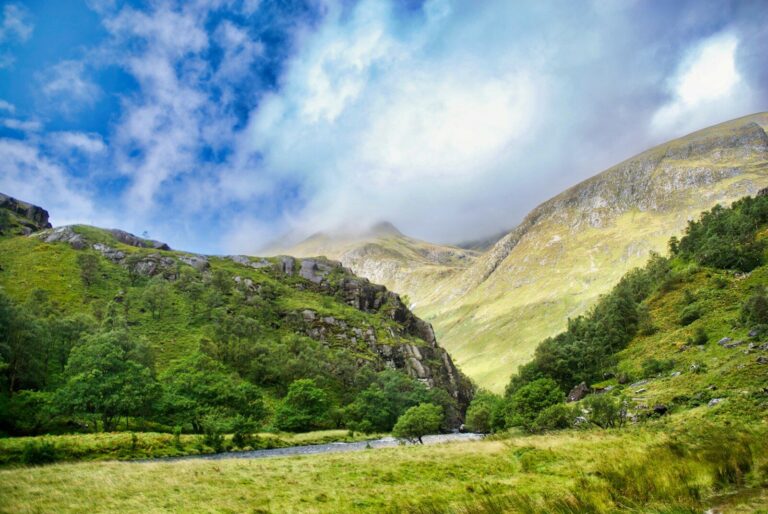 Lush green valley with mountains under cloudy sky
